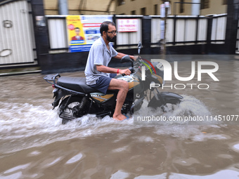 A man is riding a bike in a waterlogged street after heavy rains in Kolkata, India, on August 3, 2024. (