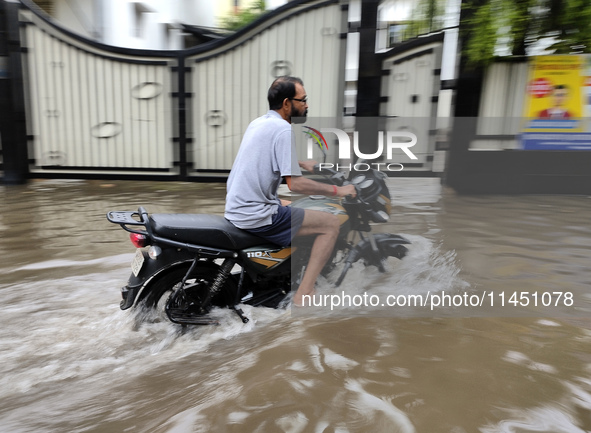 A man is riding a bike in a waterlogged street after heavy rains in Kolkata, India, on August 3, 2024. 