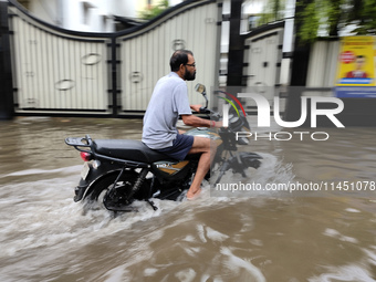 A man is riding a bike in a waterlogged street after heavy rains in Kolkata, India, on August 3, 2024. (