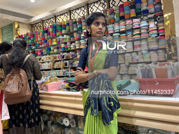 A salesgirl is standing by shelves filled with fabric borders used to make saree blouses at a textile shop in Thiruvananthapuram, Kerala, In...