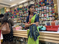 A salesgirl is standing by shelves filled with fabric borders used to make saree blouses at a textile shop in Thiruvananthapuram, Kerala, In...