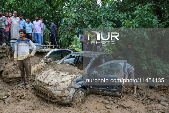 A man is using a shovel to remove debris as vehicles remain buried after a cloudburst near Cherwan Padabal area in central Kashmir's Ganderb...