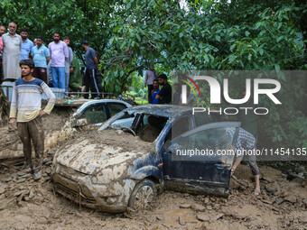 A man is using a shovel to remove debris as vehicles remain buried after a cloudburst near Cherwan Padabal area in central Kashmir's Ganderb...