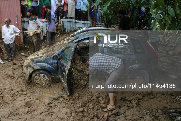 A man is using a shovel to remove debris as vehicles remain buried after a cloudburst near Cherwan Padabal area in central Kashmir's Ganderb...