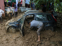 A man is using a shovel to remove debris as vehicles remain buried after a cloudburst near Cherwan Padabal area in central Kashmir's Ganderb...