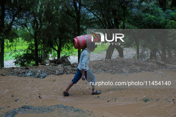 A man is carrying a gas cylinder as he walks over the debris after a cloudburst near Cherwan Padabal area in central Kashmir's Ganderbal dis...