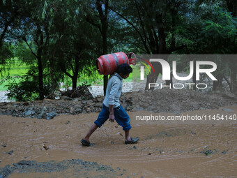 A man is carrying a gas cylinder as he walks over the debris after a cloudburst near Cherwan Padabal area in central Kashmir's Ganderbal dis...