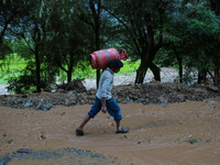 A man is carrying a gas cylinder as he walks over the debris after a cloudburst near Cherwan Padabal area in central Kashmir's Ganderbal dis...