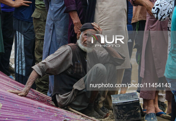 An elderly man is looking on as excavators are removing debris after a cloudburst near Cherwan Padabal area in central Kashmir's Ganderbal d...