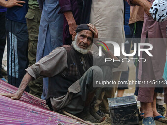 An elderly man is looking on as excavators are removing debris after a cloudburst near Cherwan Padabal area in central Kashmir's Ganderbal d...