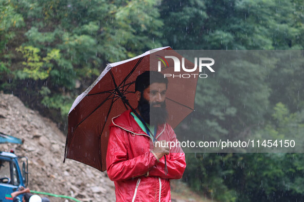 A man is holding an umbrella as he looks on while excavators are removing debris after a cloudburst near Cherwan Padabal area in central Kas...