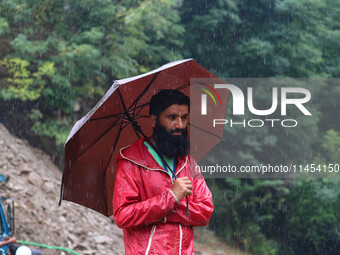 A man is holding an umbrella as he looks on while excavators are removing debris after a cloudburst near Cherwan Padabal area in central Kas...