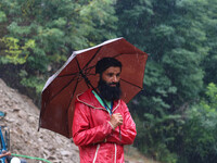 A man is holding an umbrella as he looks on while excavators are removing debris after a cloudburst near Cherwan Padabal area in central Kas...