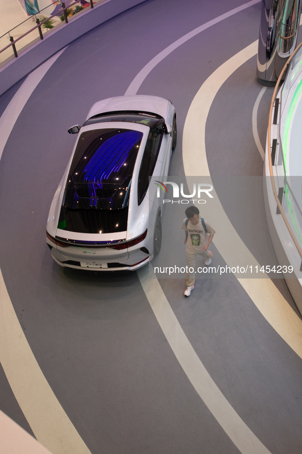 A man is walking past a BYD auto as 70 models from auto dealers like Tesla, Audi, Hongqi, SAIC Volkswagen, and Jiyue Nio are on display duri...