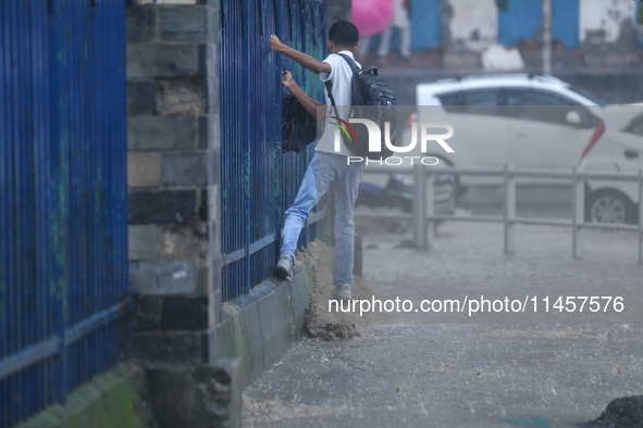 A man is taking support of the railings to get across the flooded section of road in Kathmandu, Nepal, on August 6, 2024. Nepal's Meteorolog...