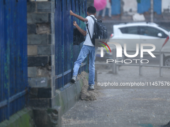 A man is taking support of the railings to get across the flooded section of road in Kathmandu, Nepal, on August 6, 2024. Nepal's Meteorolog...