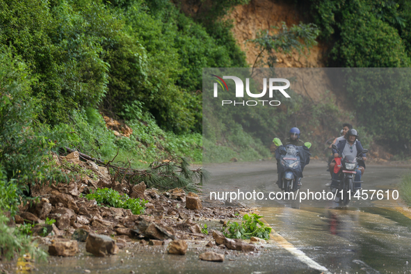 Motorcyclists are driving next to the landslide that came down in Chovar of Kathmandu, Nepal, on August 6, 2024, after incessant rainfall ov...