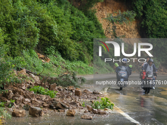 Motorcyclists are driving next to the landslide that came down in Chovar of Kathmandu, Nepal, on August 6, 2024, after incessant rainfall ov...