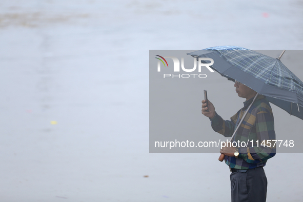 A man is taking a photo on his phone, recording the swollen Bagmati River on the embankments of Bagmati River in Teku of Kathmandu, Nepal, o...