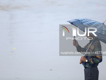 A man is taking a photo on his phone, recording the swollen Bagmati River on the embankments of Bagmati River in Teku of Kathmandu, Nepal, o...