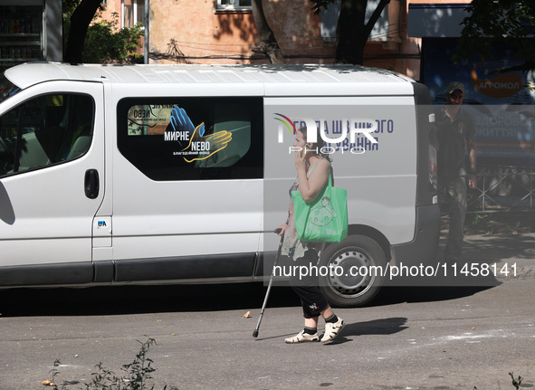 A woman is talking on the phone and walking with the help of a cane crutch past a rapid response van after the Russian rocket attack in Khar...