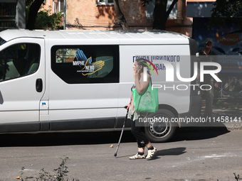 A woman is talking on the phone and walking with the help of a cane crutch past a rapid response van after the Russian rocket attack in Khar...