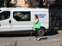 A woman is talking on the phone and walking with the help of a cane crutch past a rapid response van after the Russian rocket attack in Khar...