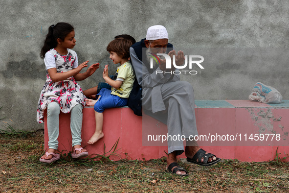 An elderly man is raising his hands during supplication as kids are playing while Muslim devotees (not in picture) are taking part in Salatu...