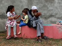 An elderly man is raising his hands during supplication as kids are playing while Muslim devotees (not in picture) are taking part in Salatu...