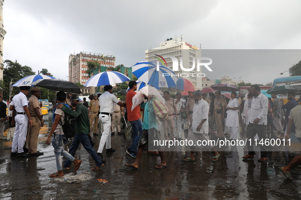 Police officers are holding umbrellas as commuters are walking past during monsoon rain in Kolkata, India, on July 07, 2024. 