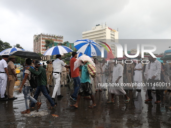 Police officers are holding umbrellas as commuters are walking past during monsoon rain in Kolkata, India, on July 07, 2024. (