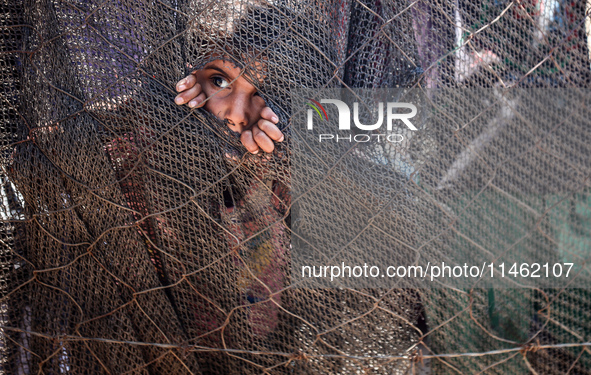 A girl is looking as Palestinians are gathering to receive food cooked by a charity kitchen, amid shortages of aid supplies, as the conflict...