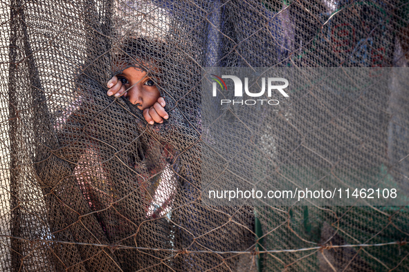 A girl is looking as Palestinians are gathering to receive food cooked by a charity kitchen, amid shortages of aid supplies, as the conflict...