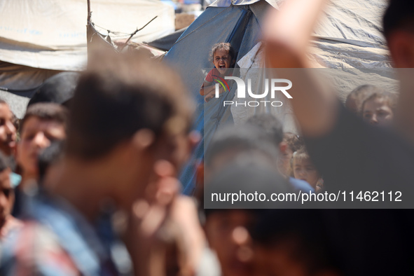 A girl is looking as Palestinians are gathering to receive food cooked by a charity kitchen, amid shortages of aid supplies, as the conflict...