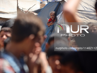 A girl is looking as Palestinians are gathering to receive food cooked by a charity kitchen, amid shortages of aid supplies, as the conflict...