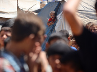 A girl is looking as Palestinians are gathering to receive food cooked by a charity kitchen, amid shortages of aid supplies, as the conflict...