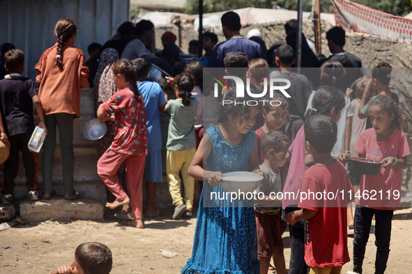 Displaced Palestinians are gathering to receive food cooked by a charity kitchen, amid food scarcity, as the Israel-Hamas conflict continues...