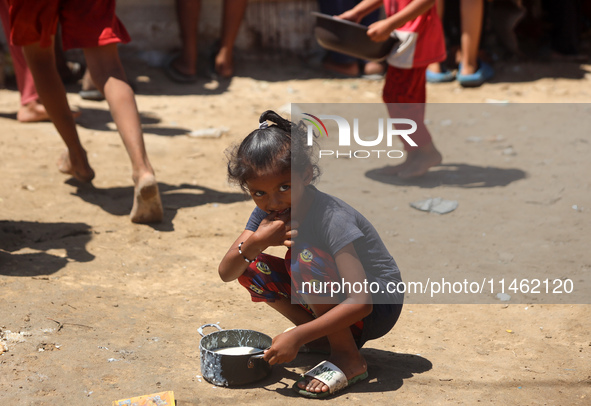 A girl is sitting as Palestinians are gathering to receive food cooked by a charity kitchen, amid shortages of aid supplies, as the conflict...