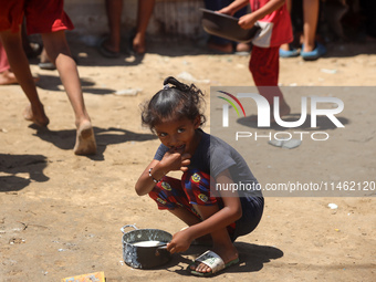 A girl is sitting as Palestinians are gathering to receive food cooked by a charity kitchen, amid shortages of aid supplies, as the conflict...