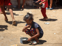 A girl is sitting as Palestinians are gathering to receive food cooked by a charity kitchen, amid shortages of aid supplies, as the conflict...