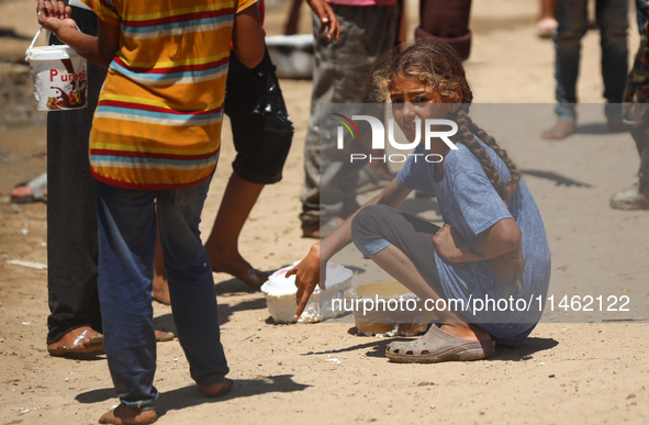 A girl is sitting as Palestinians are gathering to receive food cooked by a charity kitchen, amid shortages of aid supplies, as the conflict...