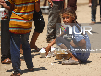 A girl is sitting as Palestinians are gathering to receive food cooked by a charity kitchen, amid shortages of aid supplies, as the conflict...