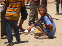 A girl is sitting as Palestinians are gathering to receive food cooked by a charity kitchen, amid shortages of aid supplies, as the conflict...