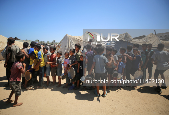 Displaced Palestinians are gathering to receive food cooked by a charity kitchen, amid food scarcity, as the Israel-Hamas conflict continues...