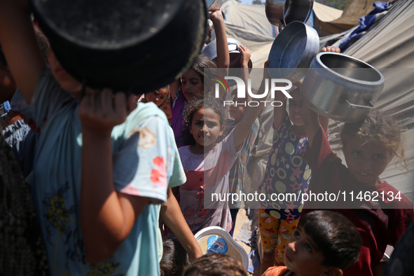 Displaced Palestinians are gathering to receive food cooked by a charity kitchen, amid food scarcity, as the Israel-Hamas conflict continues...