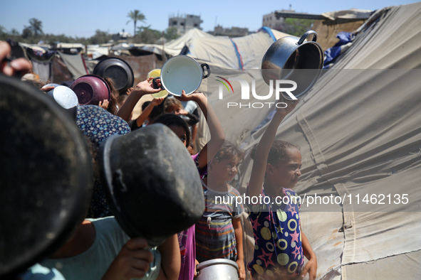 Displaced Palestinians are gathering to receive food cooked by a charity kitchen, amid food scarcity, as the Israel-Hamas conflict continues...