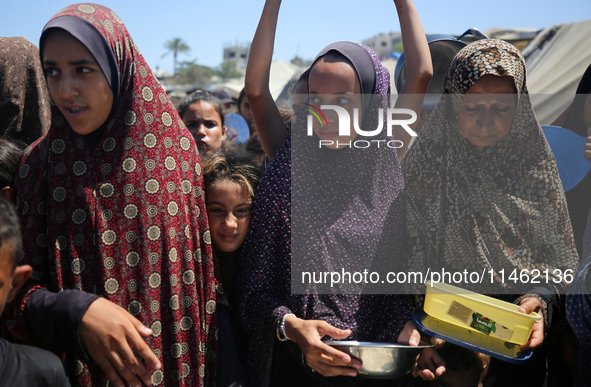 Displaced Palestinians are gathering to receive food cooked by a charity kitchen, amid food scarcity, as the Israel-Hamas conflict continues...