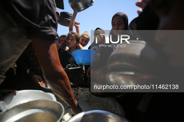 Displaced Palestinians are gathering to receive food cooked by a charity kitchen, amid food scarcity, as the Israel-Hamas conflict continues...