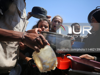 Displaced Palestinians are gathering to receive food cooked by a charity kitchen, amid food scarcity, as the Israel-Hamas conflict continues...