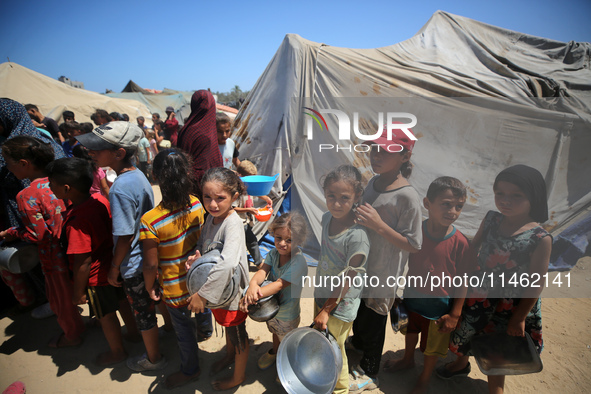 Displaced Palestinians are gathering to receive food cooked by a charity kitchen, amid food scarcity, as the Israel-Hamas conflict continues...